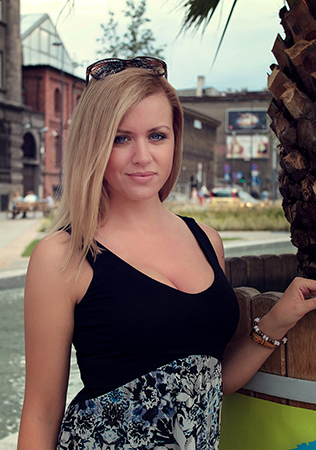 A blonde girl with blue eyes posing next to phoenix plant.