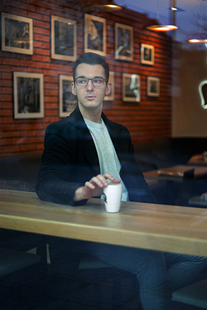 A young man enjoying his coffee behind a cafe window.