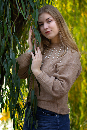 Portrait of a blonde girl holding a tree brunch full of leaves.