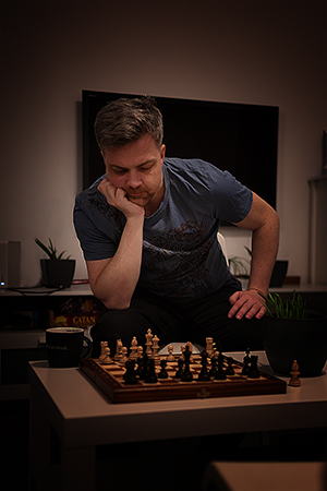 A young man playing chess and thinking his next move, sitting in the living room.