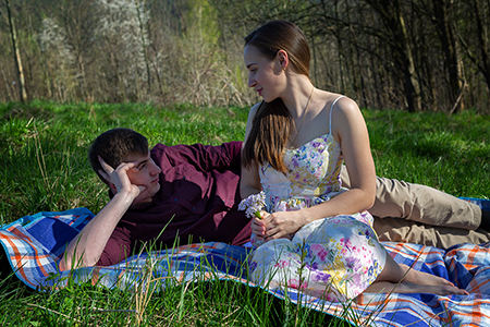 A couple sitting on a blanket in a green country landscape.