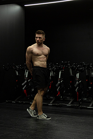 A topless musceled young man demonstrating his muscles in a dark gym room.