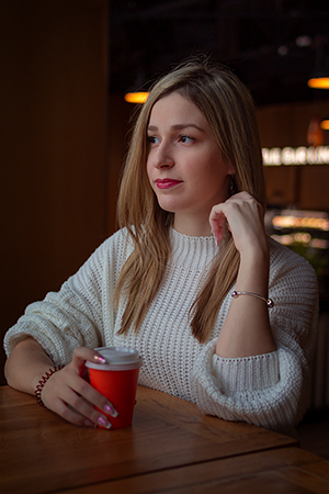 A blonde girl with white sweater enjoying a coffee in a cafe.