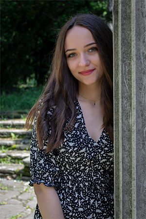 A portrait of Kamilla, smilling behind a column.