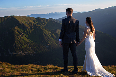 Groom holding bride by her hand, looking at the mountains.