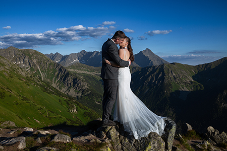 Groom is kissing the bride on a rock, at Tatra mountains under a blue sky.