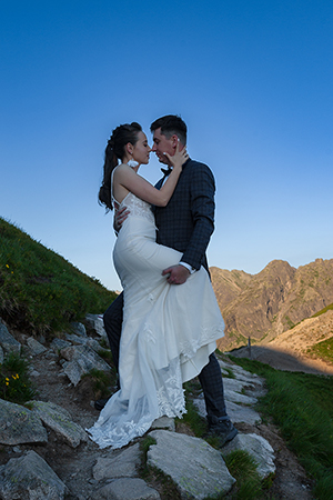 Groom is holding bridge by waste, raising her leg under the mountain shadow.