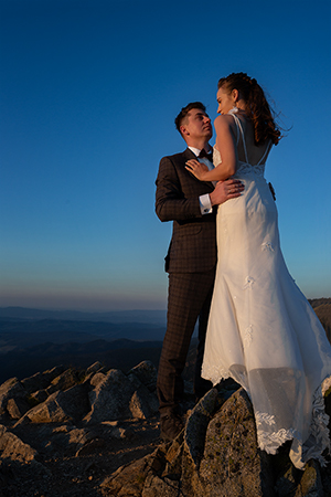 Groom hugs bride in a rocky landscape at late evening.