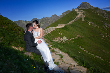 A wedding couple at Tatra mountains, sitting at the grass and huging.