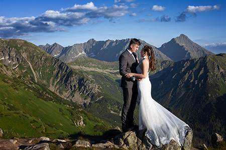 Groom and bride huging at mountains under a clear blue sky.