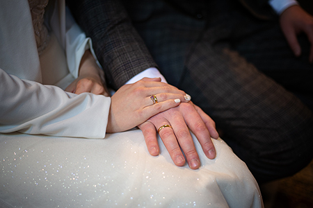 Bride's hand gently over groom's hand, wearing their wedding rings.