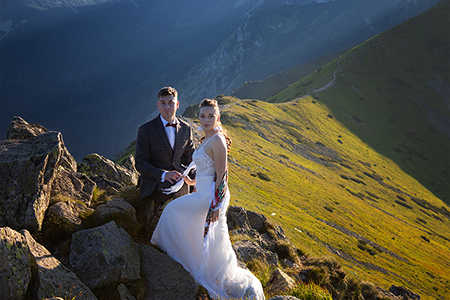 Groom and bride posing at a green mountainside.